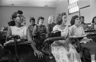 1950s high school students seated in rows in a classroom, responding to a lesson